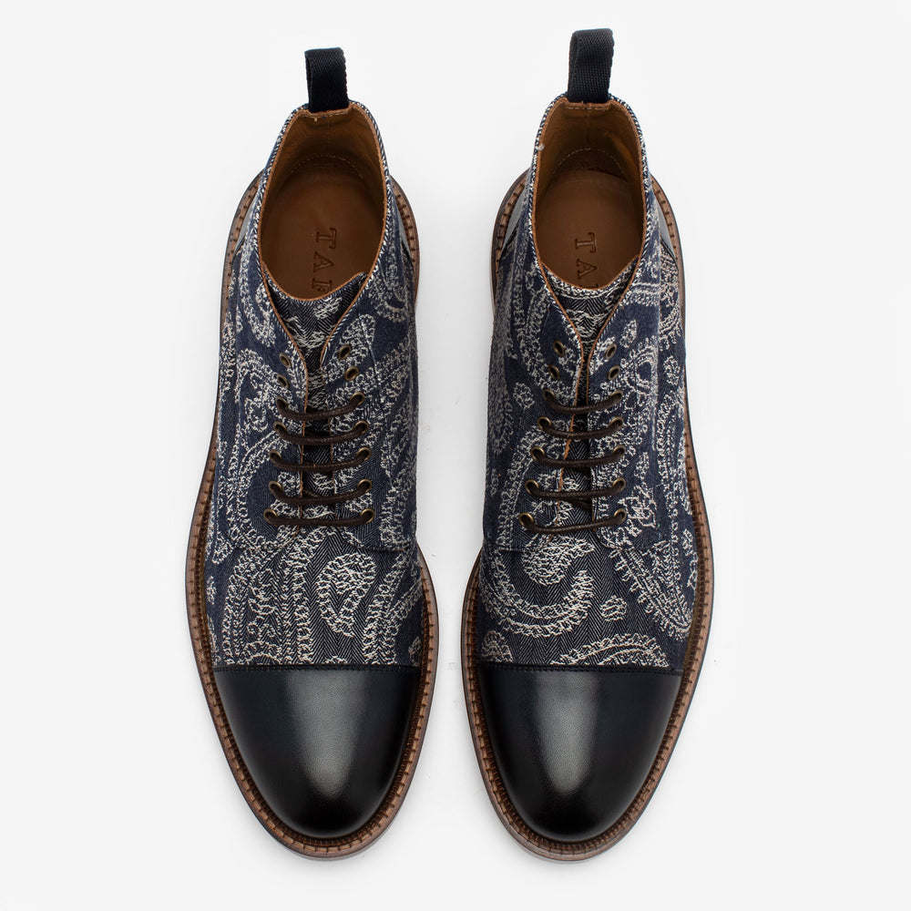 Top view of a pair of blue lace-up shoes with a paisley pattern, black leather toe caps, and brown soles.