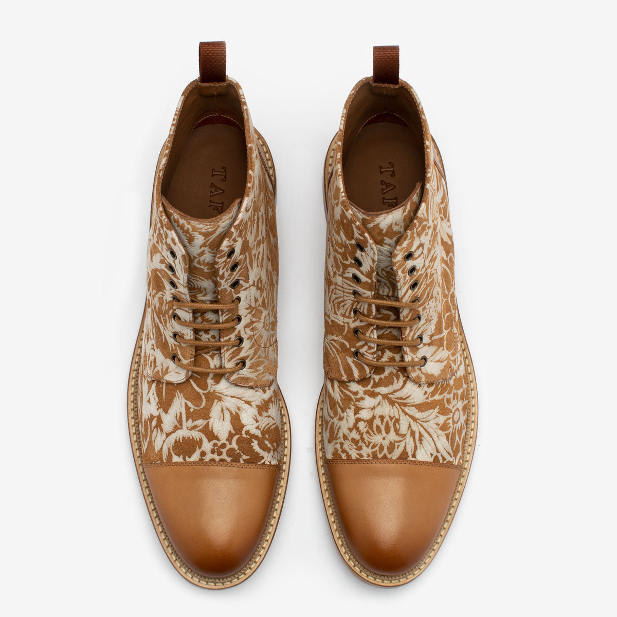 A pair of brown leather boots with floral-patterned fabric panels, laces, and a brown cap toe, viewed from above.