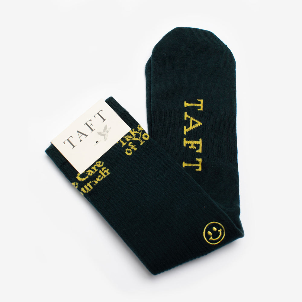 Black socks with TAFT and a smiley face on them, packaged with a white TAFT label.