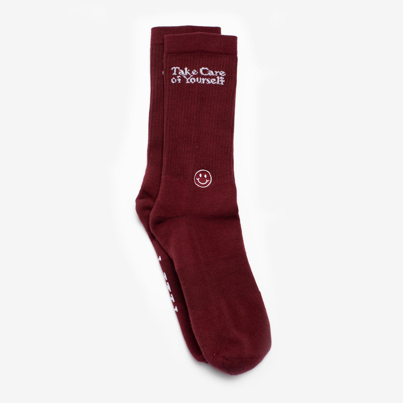 A pair of maroon socks with the message Take Care of Yourself and a small smiley face design.