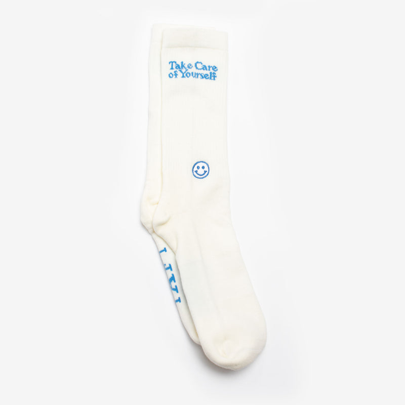 A pair of white socks with blue embroidery. One has Take Care of Yourself and a smiley face, while the other has the word I AM.