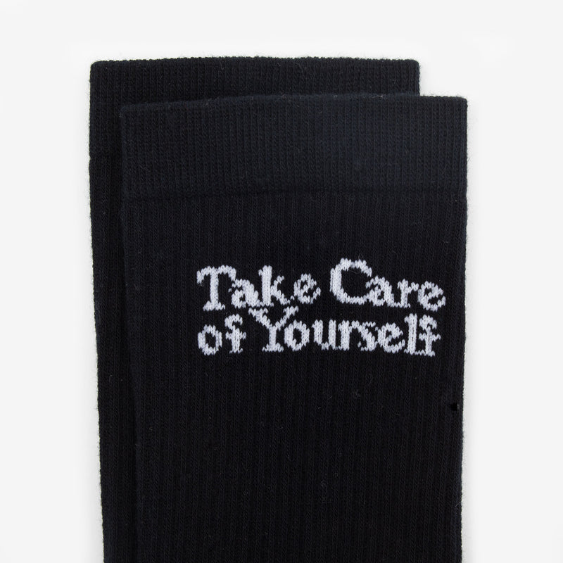 A pair of black socks with the white text Take Care of Yourself on them.