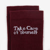 Close-up of maroon socks with the phrase Take Care of Yourself embroidered in white text near the top.