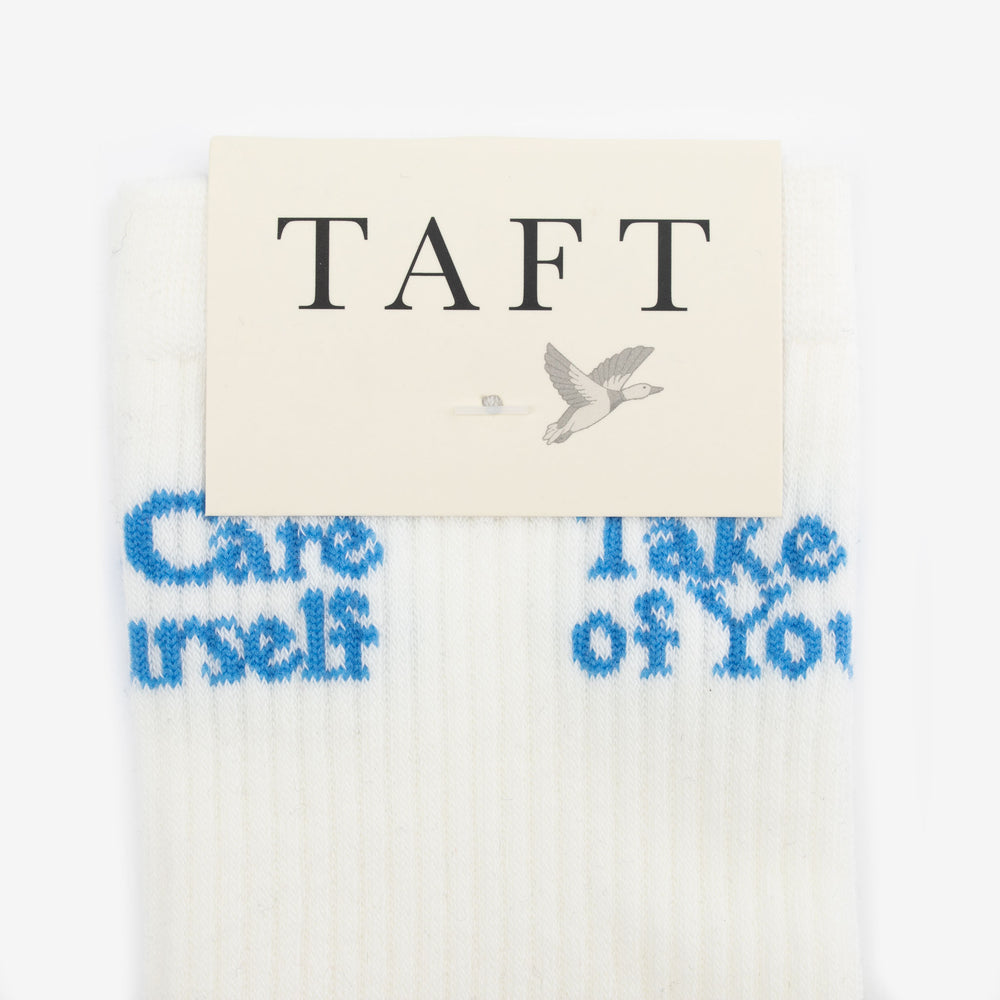 White socks with the text Care Yourself and Take Care of You in blue, packaged under a TAFT label featuring a bird graphic.