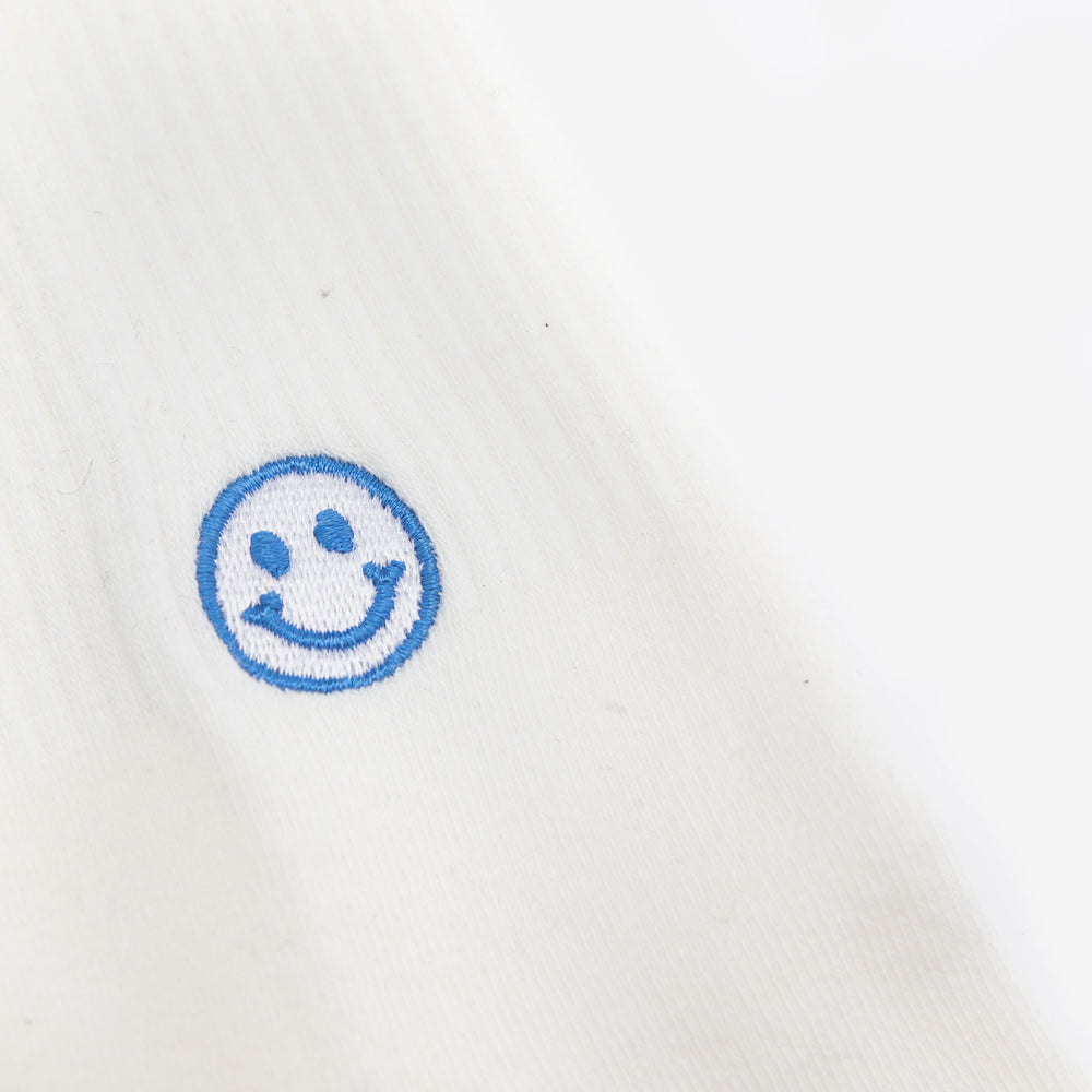 Close-up of a white fabric with a blue embroidered smiley face. The fabric appears to be smooth and clean.