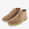 A pair of tan suede chukka boots with light brown rubber soles and beige laces, displayed on a white background.