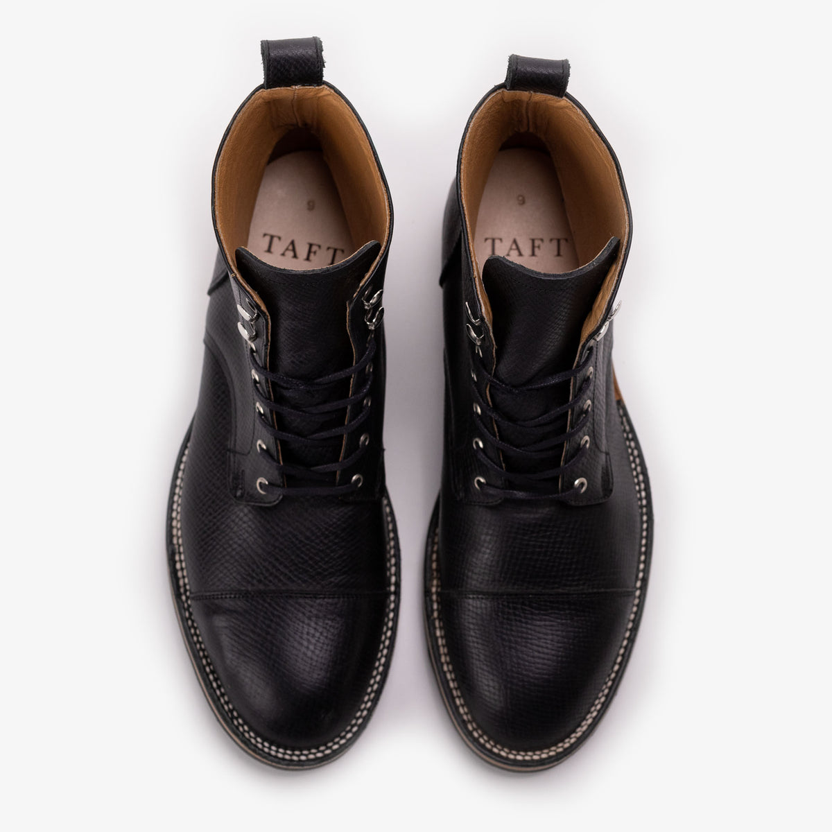 A pair of black leather lace-up boots with a textured finish, seen from above, with the word TAFT printed inside.