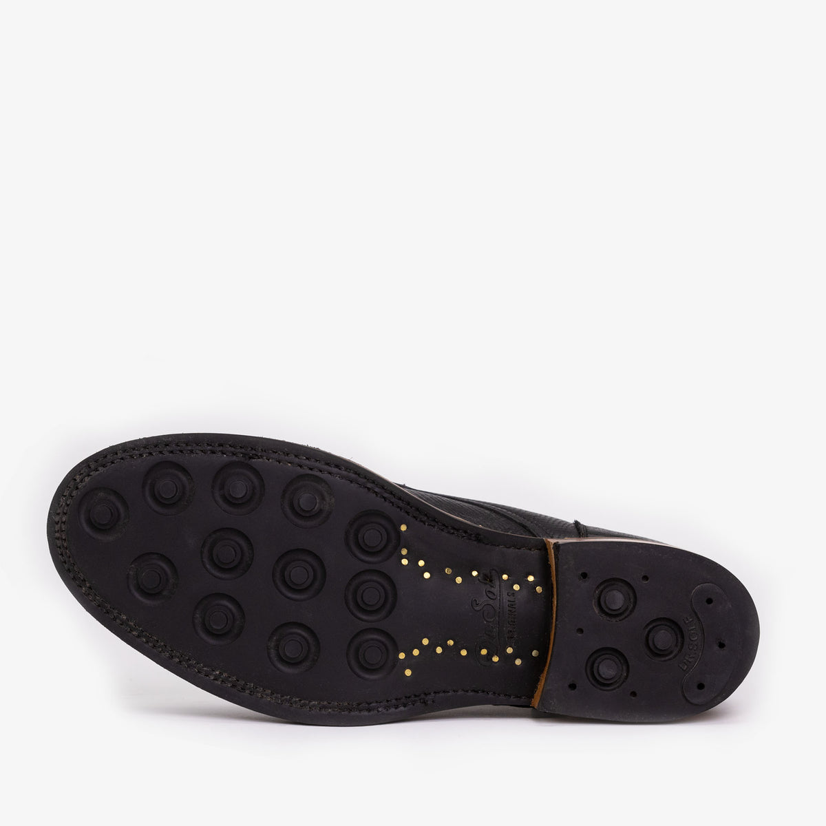 The bottom view of a black shoe with a rubber sole featuring multiple circular grip patterns and small yellow dots near the arch area.