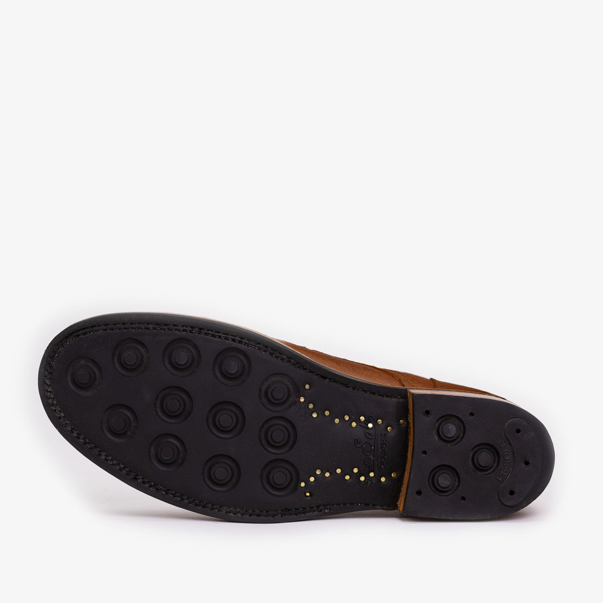 The image shows the bottom of a brown leather shoe with a black rubber sole featuring circular treads and small gold-colored accents.