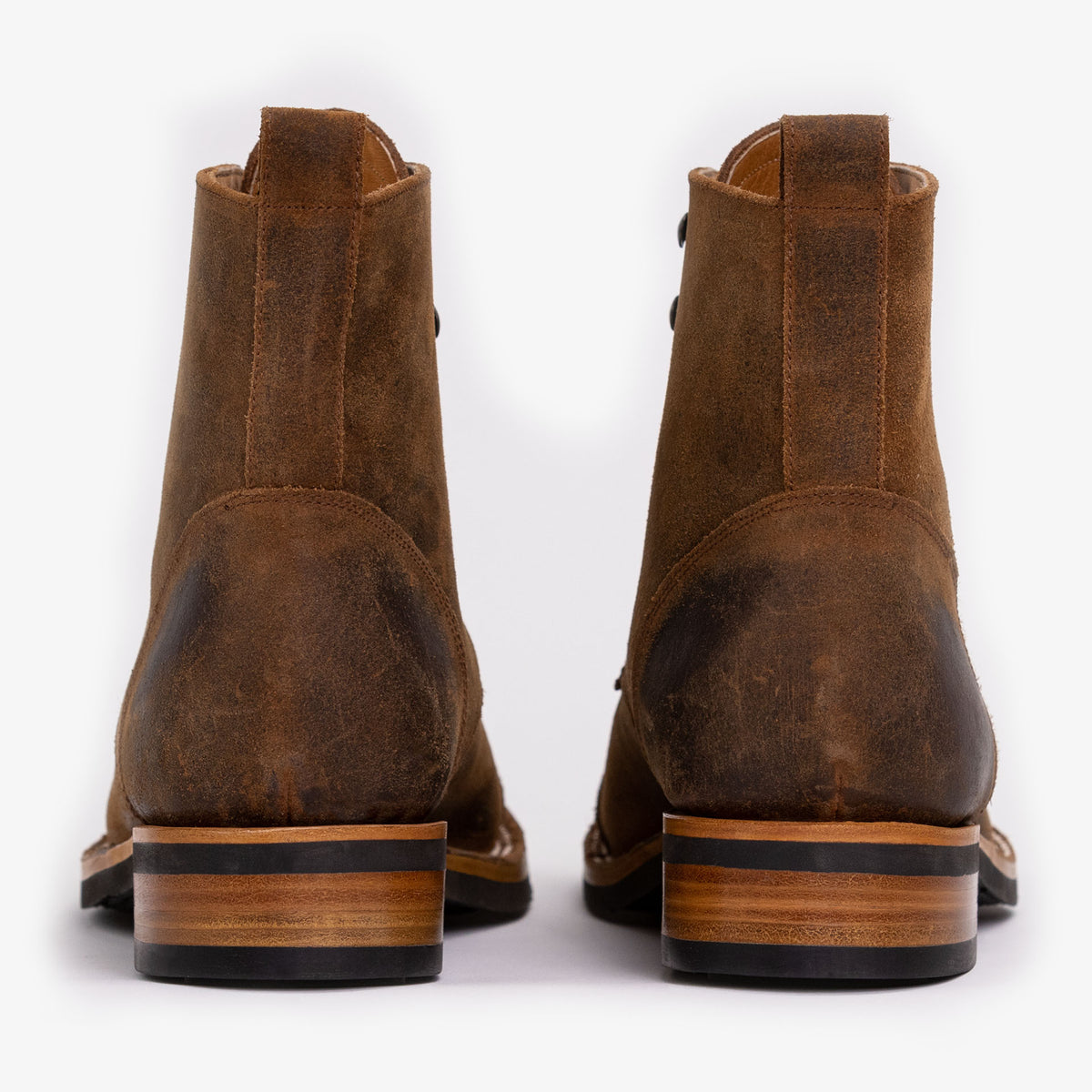 A pair of brown leather boots, shown from the back, featuring wooden block heels and black rubber soles.