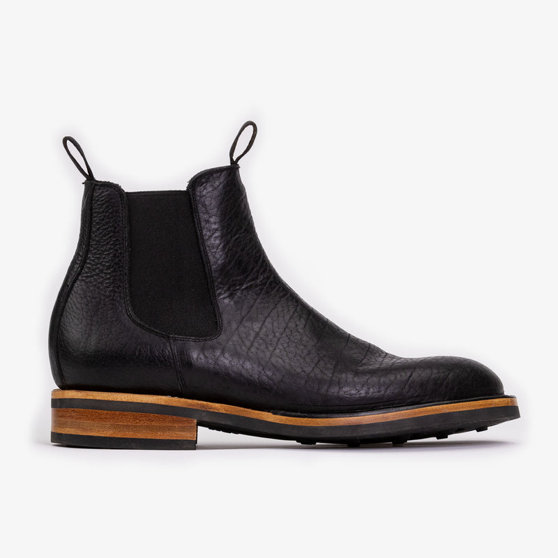 A black leather Chelsea boot with a wooden sole, elastic side panels, and pull tabs.