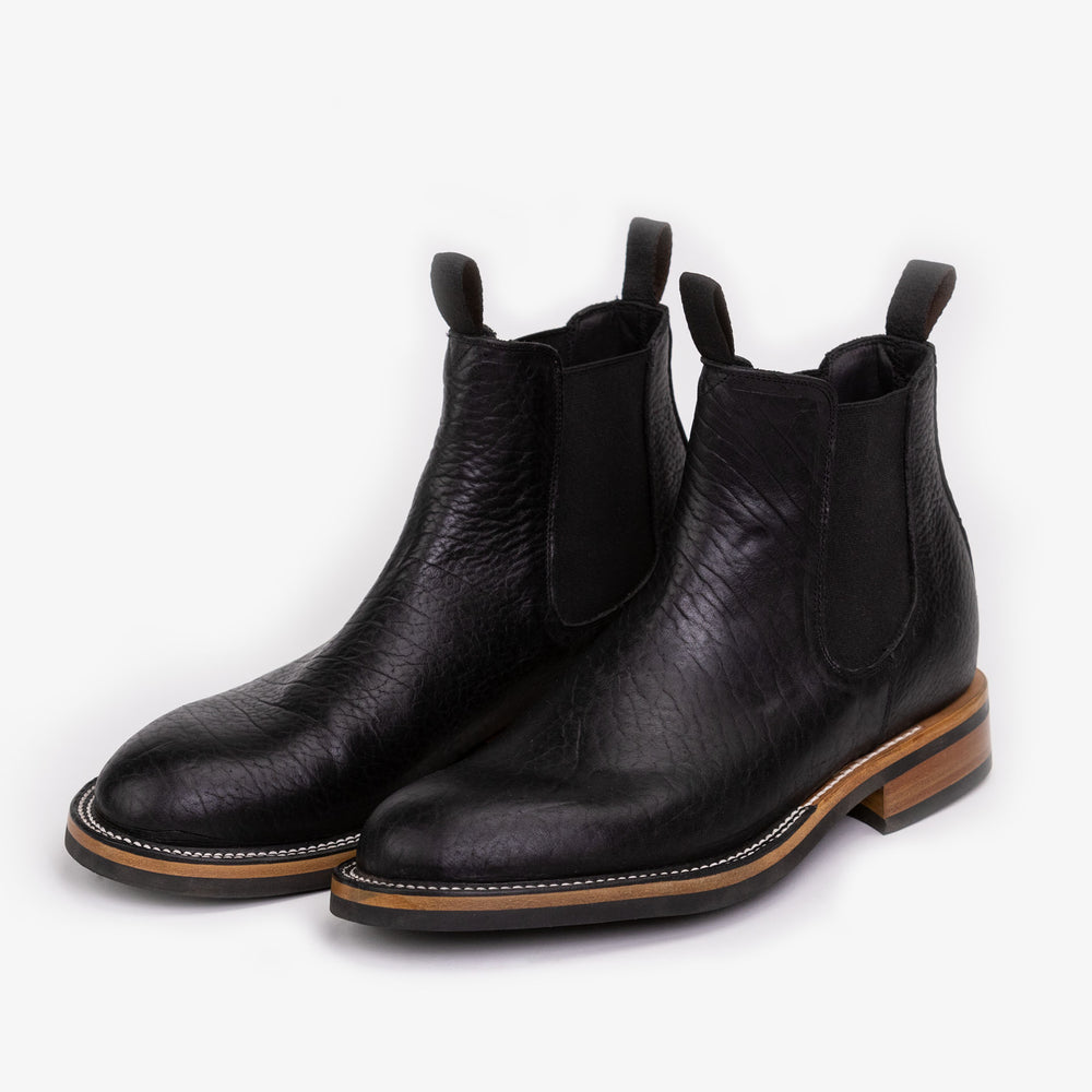 Pair of black leather Chelsea boots with elastic side panels and wooden soles, viewed from a slight angle against a white background.