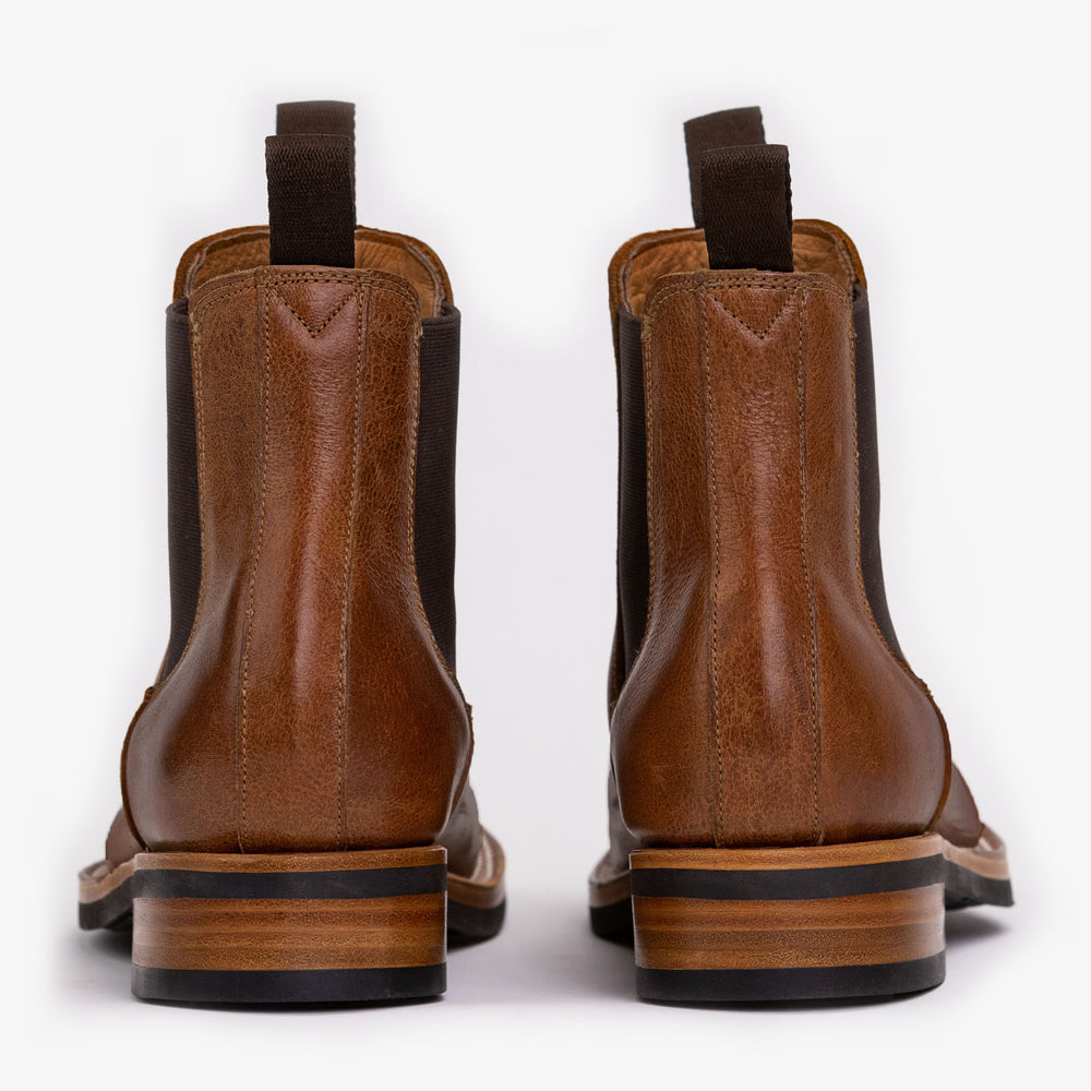 A pair of brown leather ankle boots with black elastic side panels and pull tabs, viewed from the back.