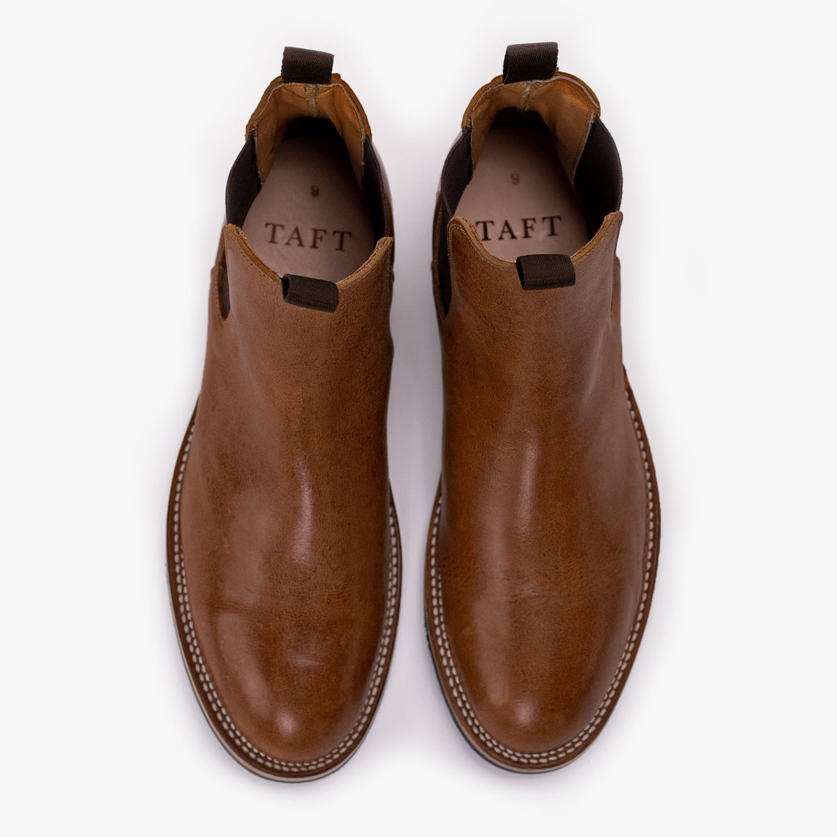 A pair of brown leather slip-on boots with the brand name TAFT on the insoles, viewed from above on a white background.