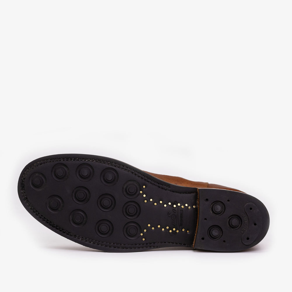 Sole of a brown leather shoe showing black rubber with circular grip patterns and small gold-colored dots along the arch.