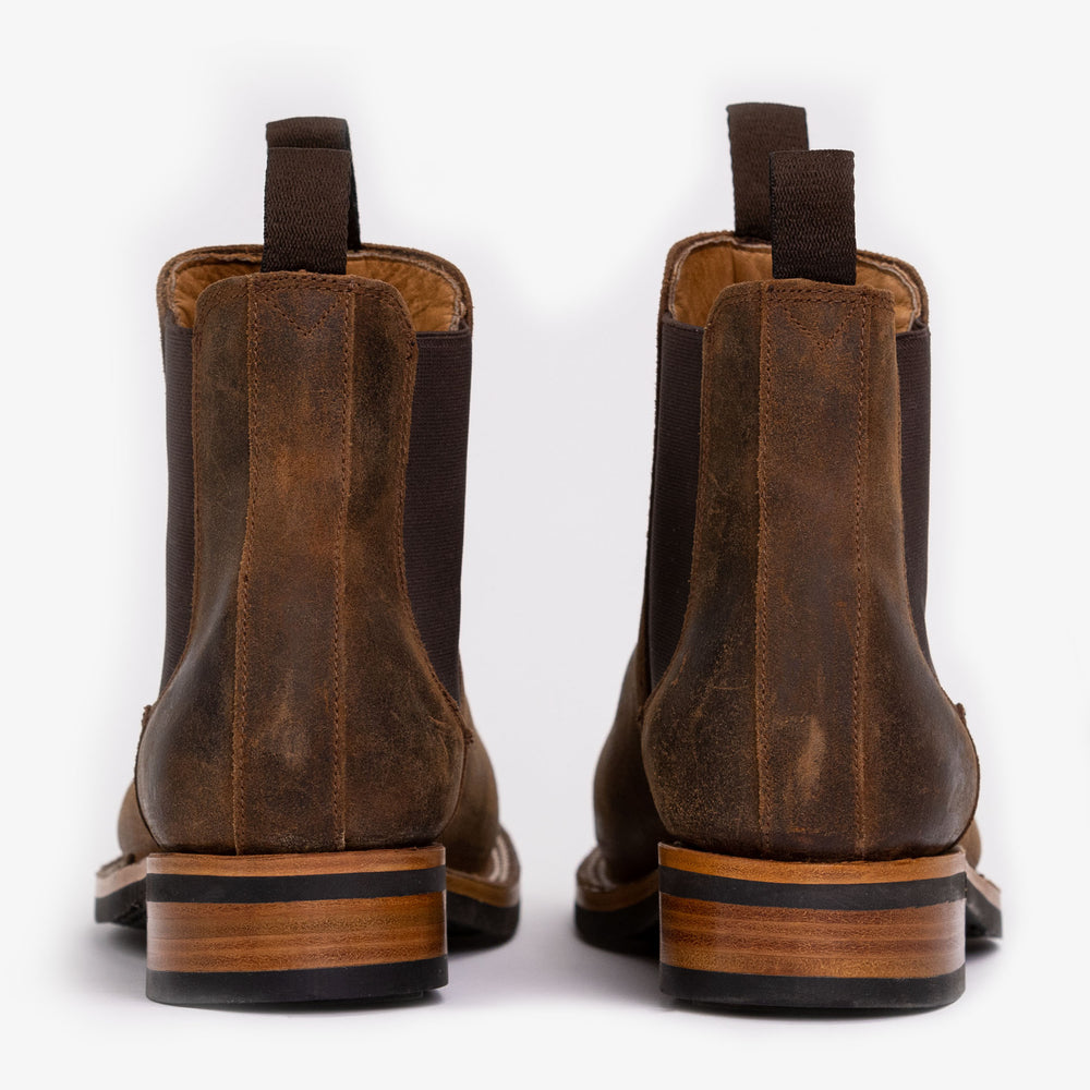 A pair of brown leather Chelsea boots viewed from the back, showcasing the wooden heels and pull tabs.