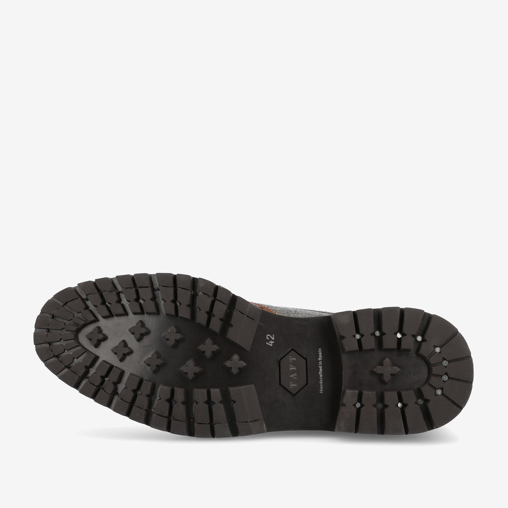 The image shows the sole of a shoe with a rugged tread pattern, featuring various geometric shapes for grip.