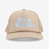 Front view of a beige trucker hat with a mesh back and the words Deep Breaths embroidered in light blue on the front panel.