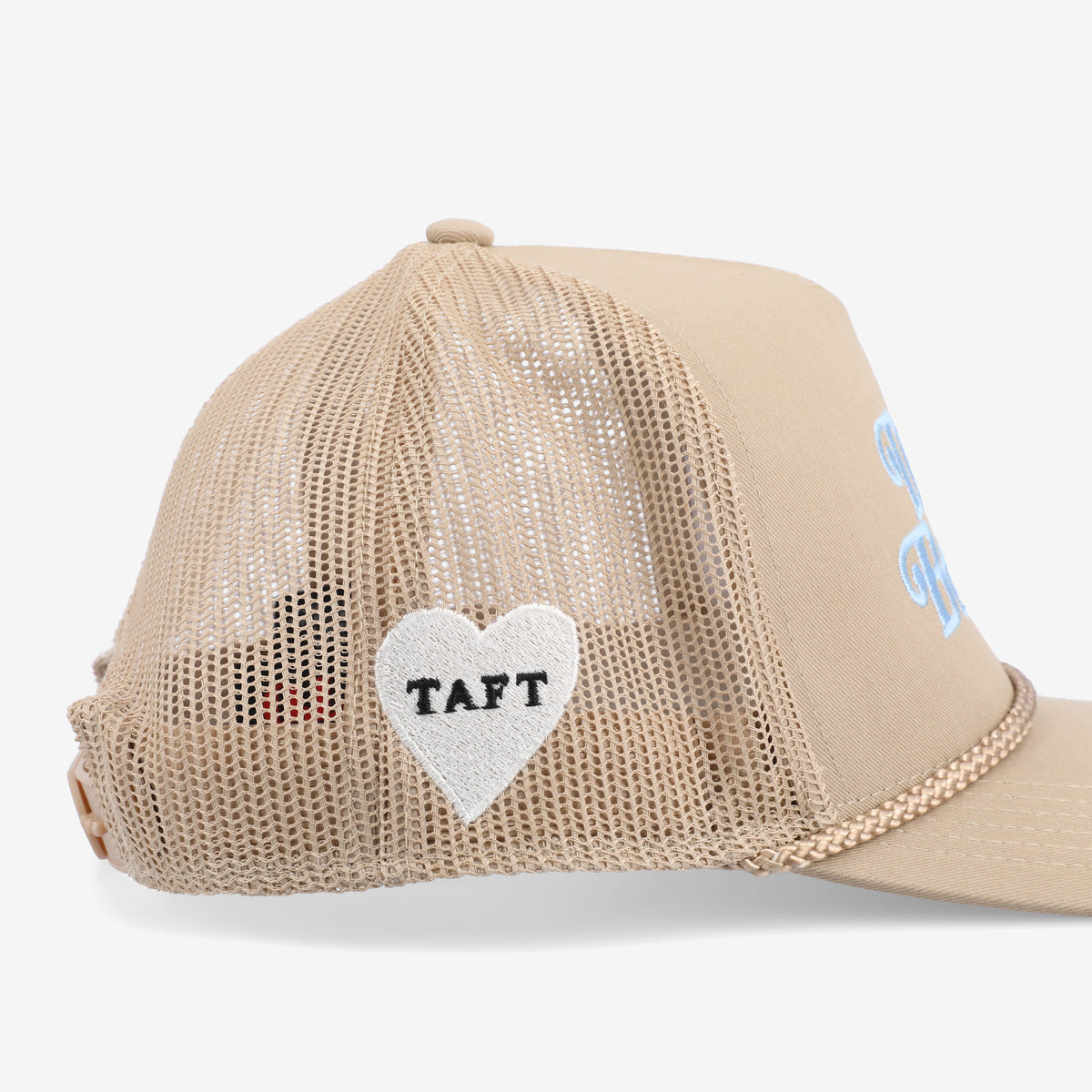 Side view of a beige trucker hat with mesh back, featuring a white heart with the word TAFT on the panel.