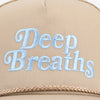 A tan hat with the words Deep Breaths embroidered in light blue on the front, and a braided trim along the edge.