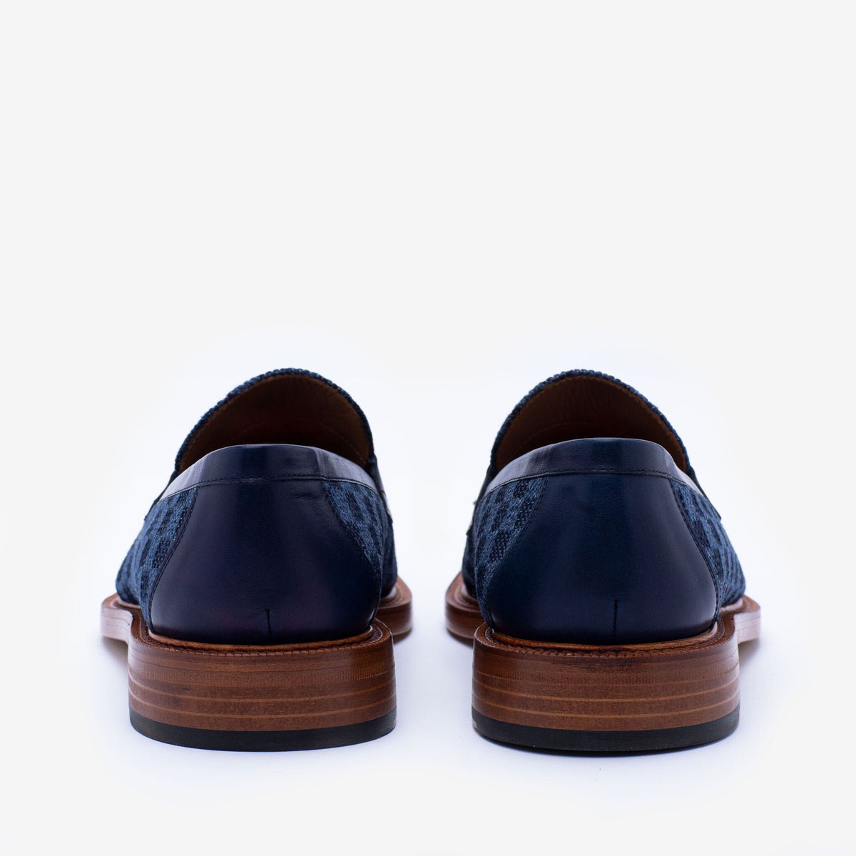 Rear view of a pair of navy blue dress shoes with dark brown wooden heels and black leather backs.