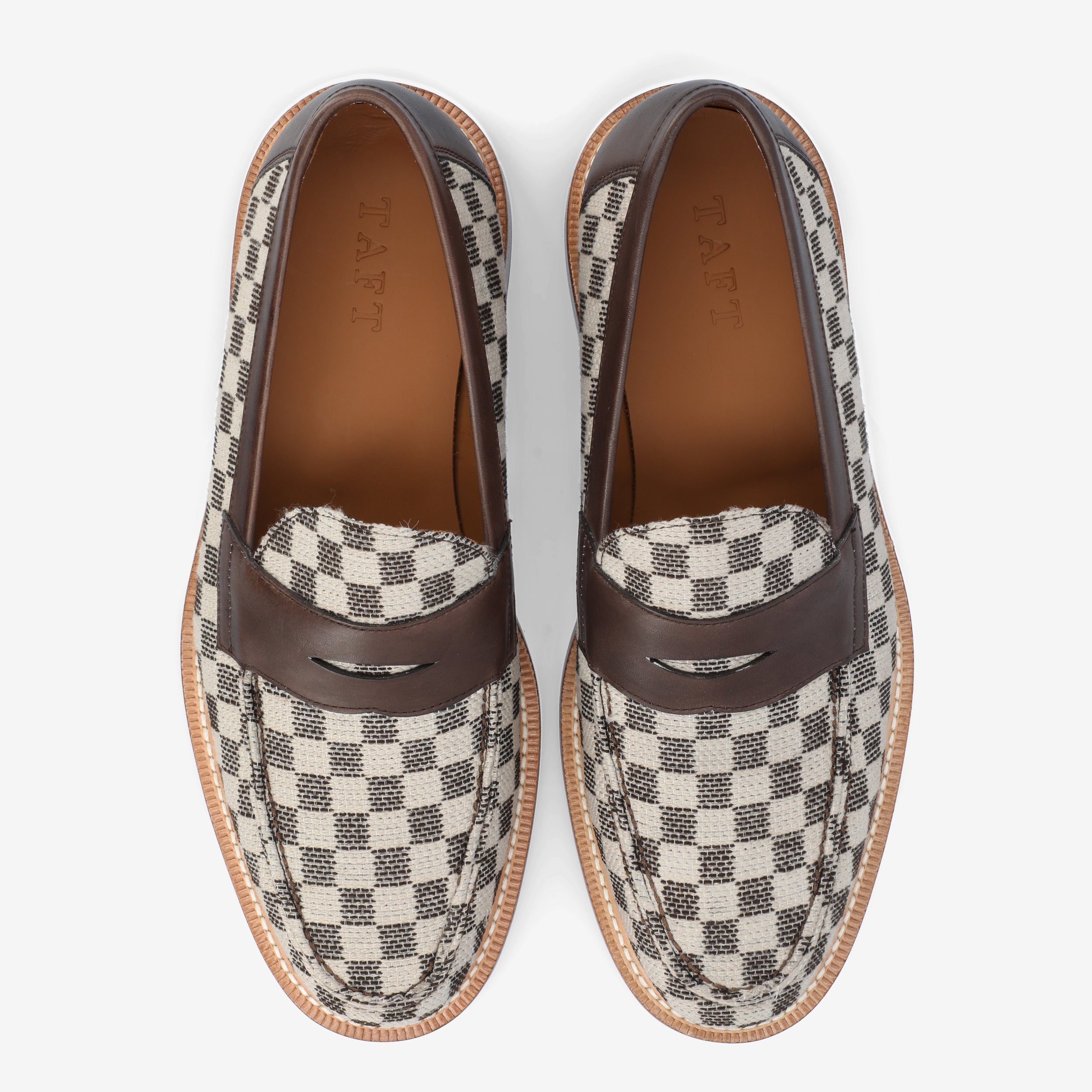 Top view of a pair of loafers featuring a black and white checkered fabric and brown leather accents.