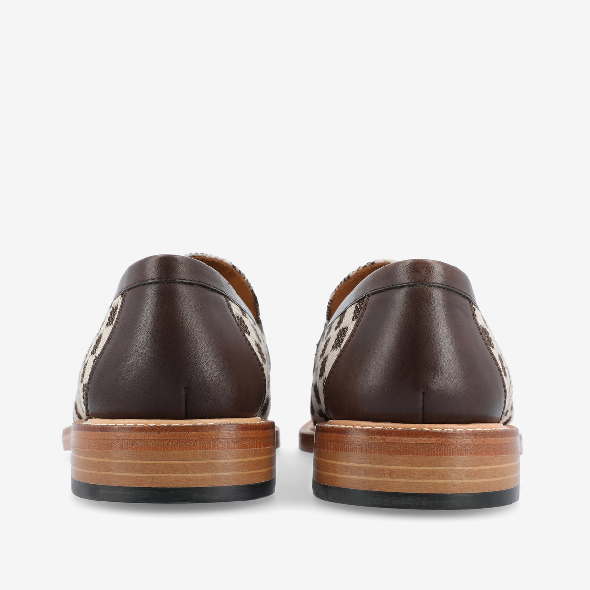 Rear view of a pair of loafers with brown leather and a woven pattern. The shoes have wooden soles with several layers.