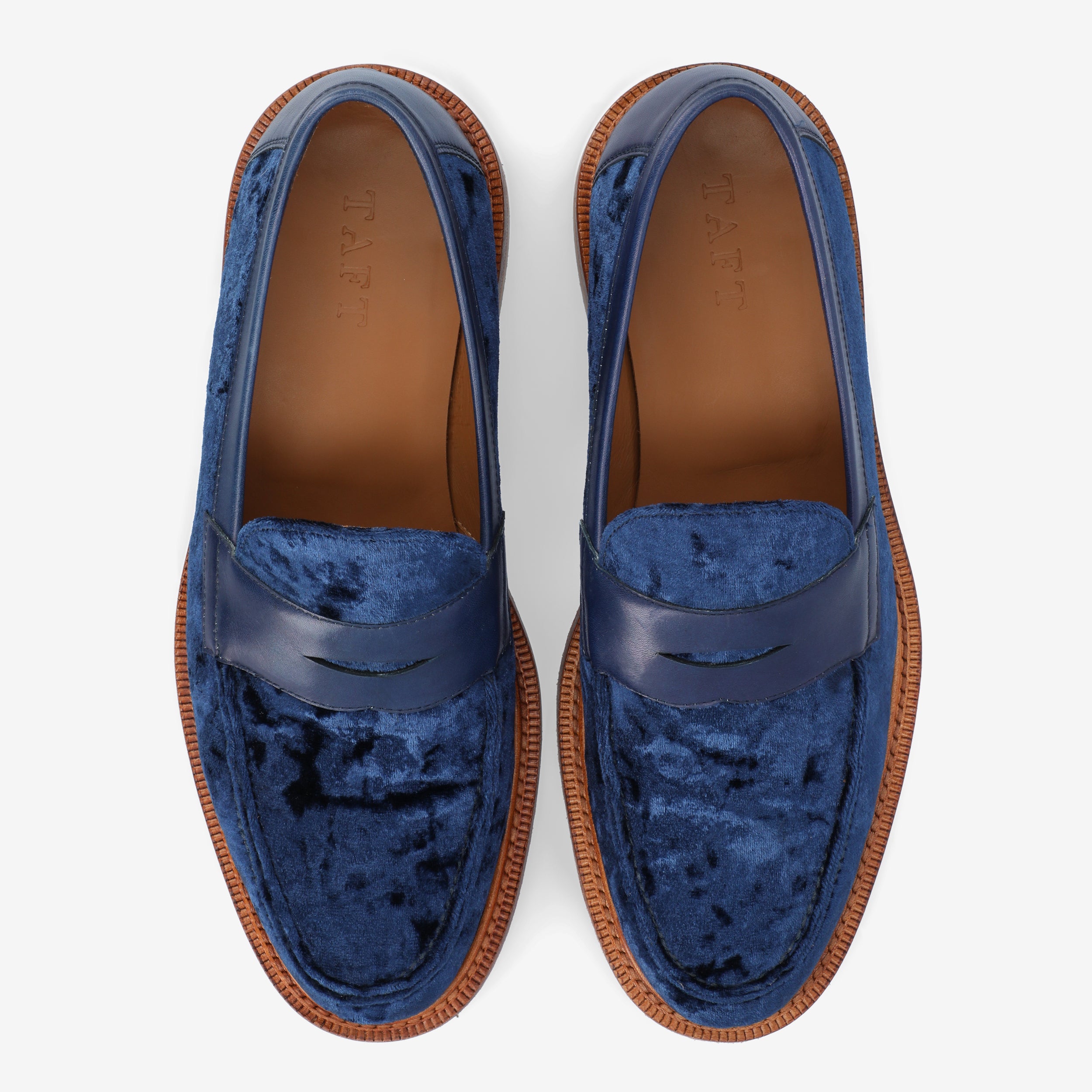 A pair of blue velvet loafers with leather accents and tan soles, viewed from above.