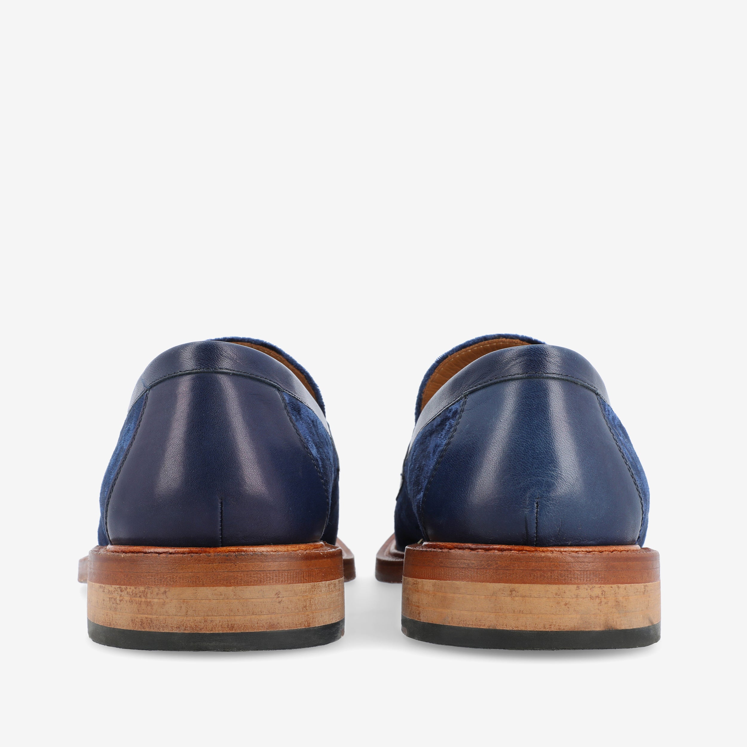 Rear view of a pair of blue loafers showcasing wooden soles with black rubber heels.