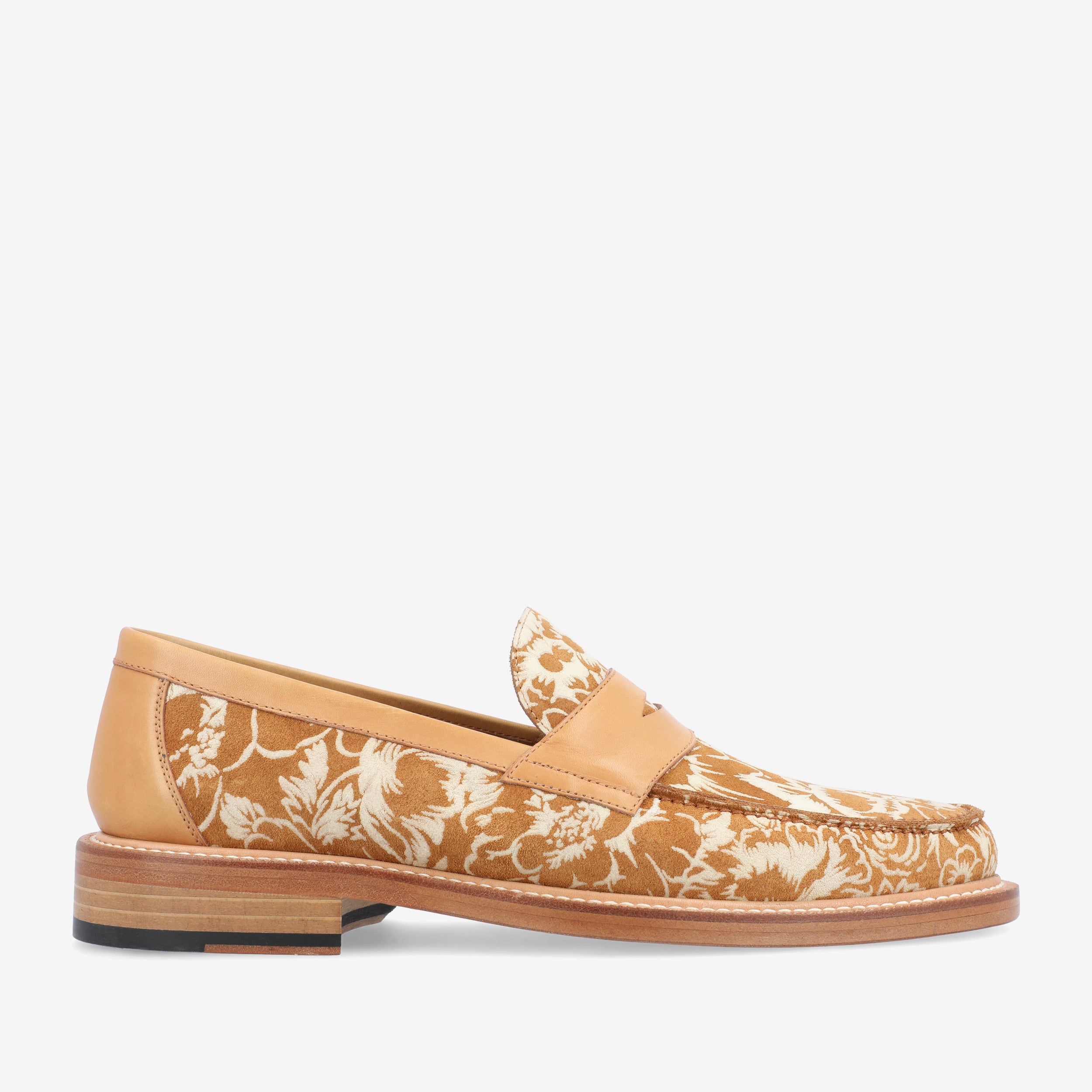 A tan leather loafer with a beige and white floral pattern, featuring a low wooden heel and a rounded toe.