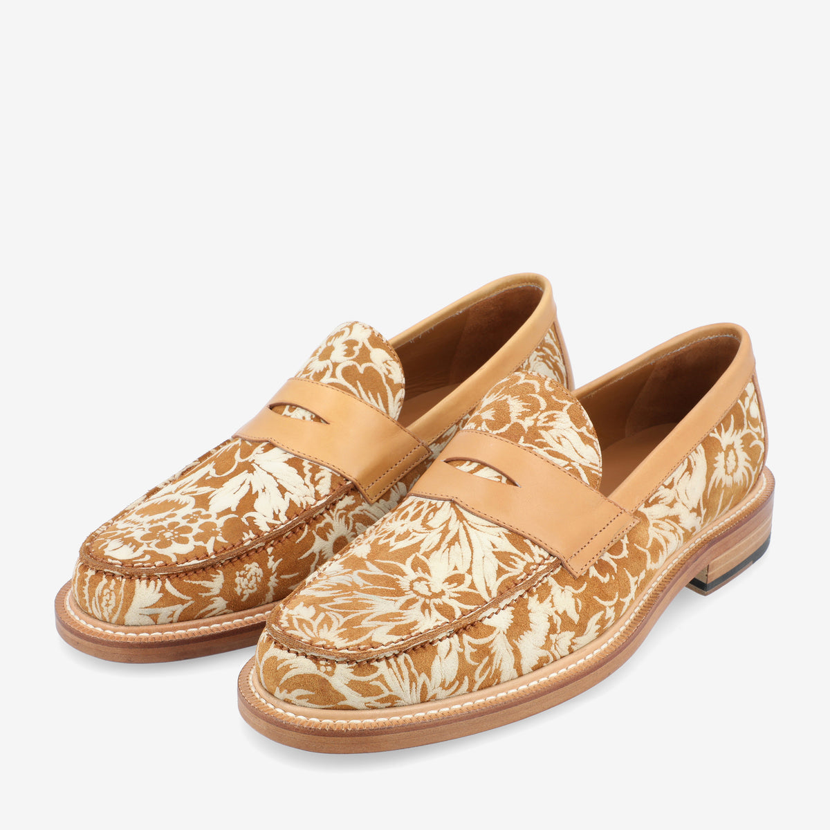 A pair of tan and white floral-patterned loafers with a leather strap detail on the top and a wooden heel.