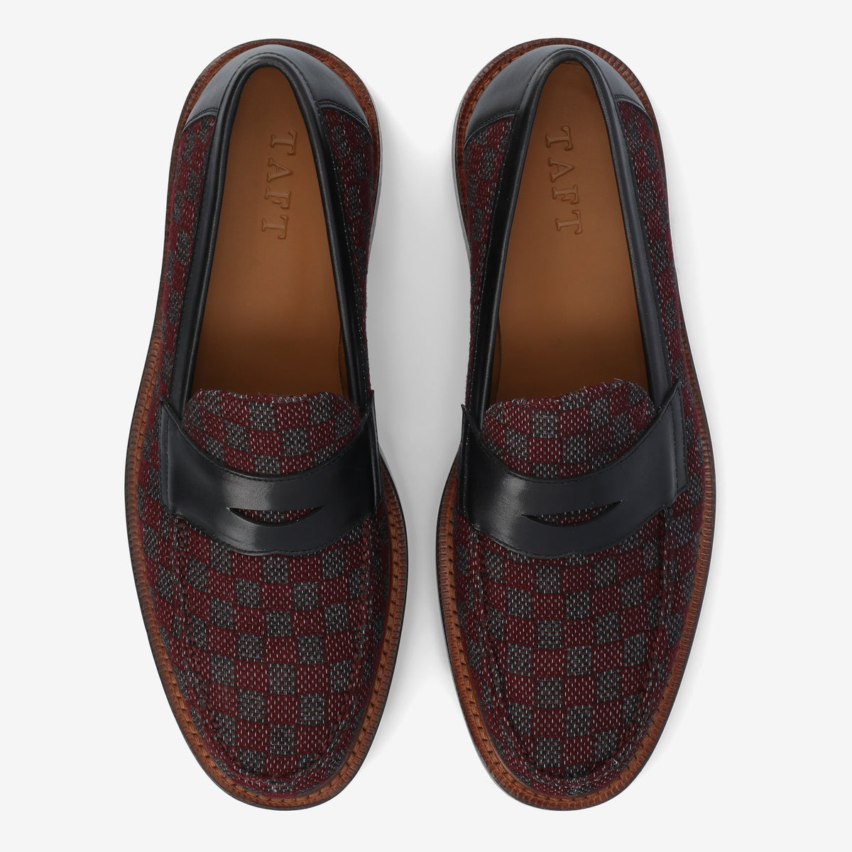 Top-down view of a pair of loafers with a red and black checkered pattern and black leather aprons, branded with TAFT on the inside sole.