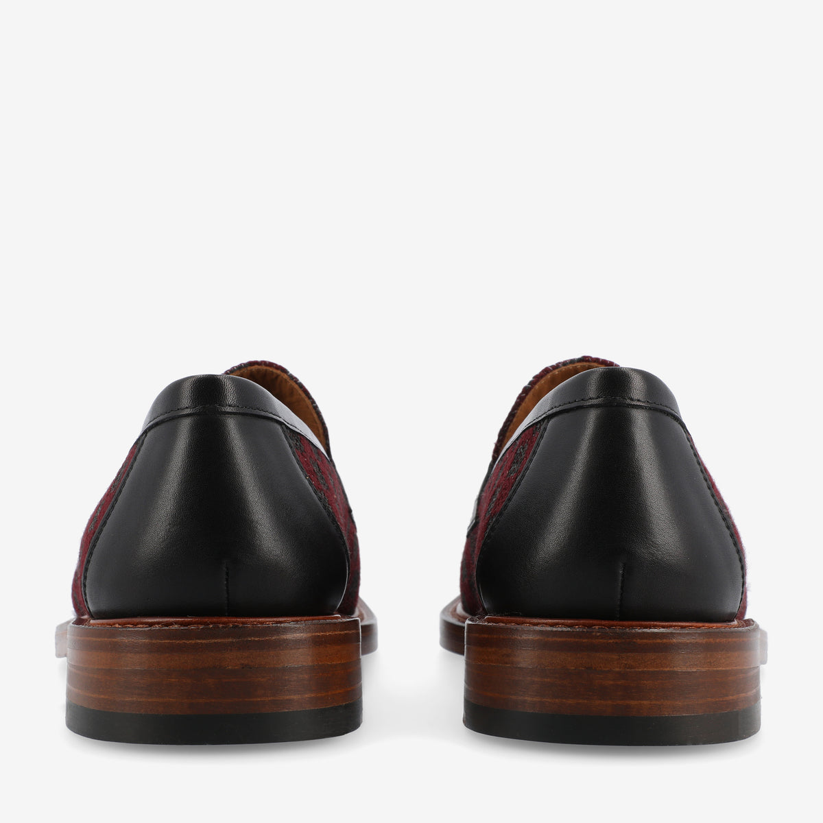 Rear view of a pair of dress shoes with black leather backs, dark brown wooden soles, and burgundy and black patterned fabric on the sides.