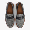 A pair of gray and black patterned loafers with brown soles, featuring a black leather strap across the top and a brown leather interior.