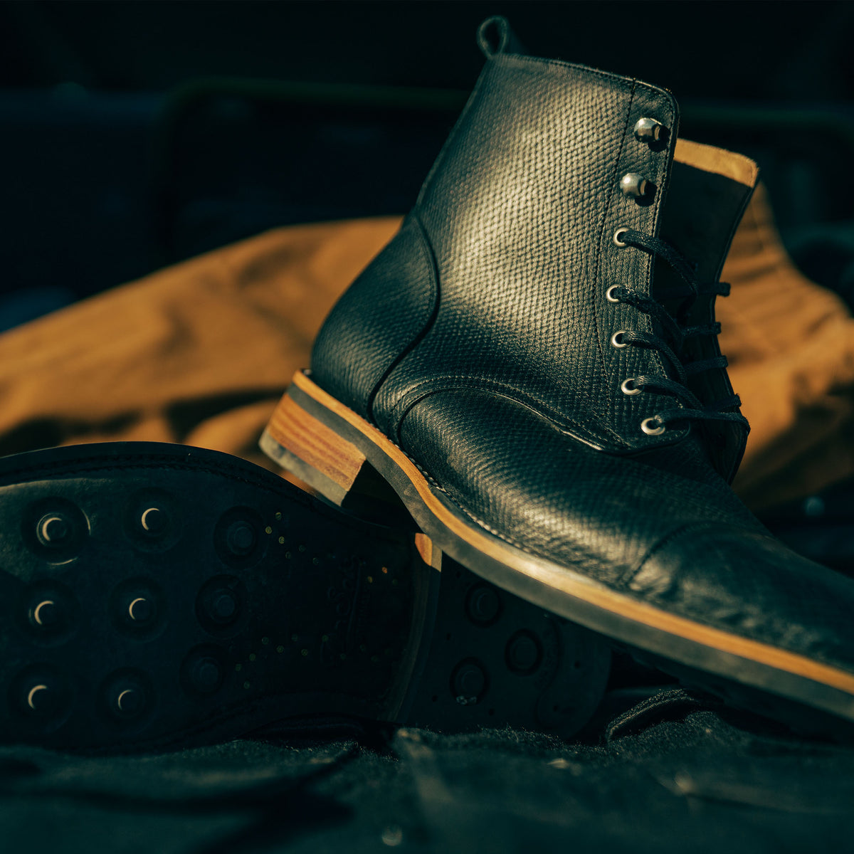 A close-up of a black leather boot with a textured surface, showing the sole and detailed stitching.