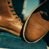 Close-up of two brown leather shoes, showing their stitching and texture, against a backdrop of blue denim.