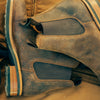 Close-up of a pair of brown leather Chelsea boots with elastic side panels and slightly worn appearance placed on a brown fabric background.