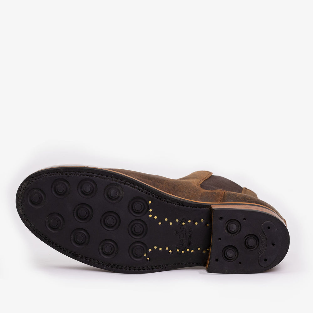 A brown leather shoe viewed from the sole, featuring black rubber material with round grips and visible stitching details.