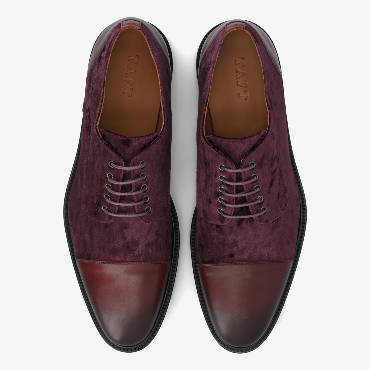 Pair of burgundy velvet and leather oxford shoes with five eyelets each and brown insoles, viewed from above.