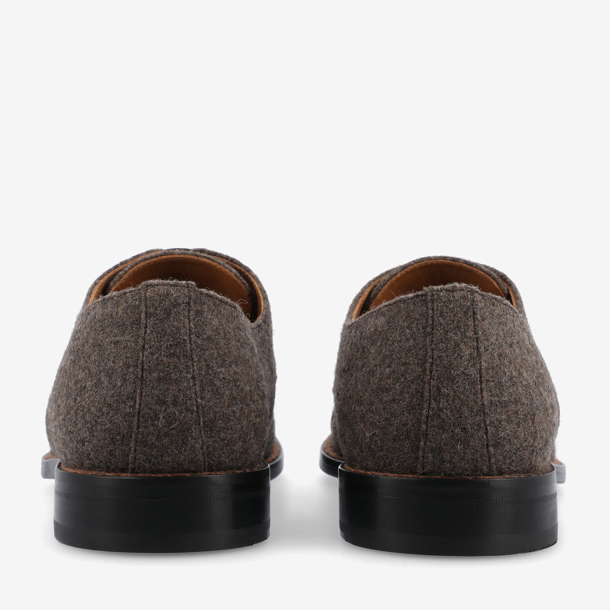 Rear view of a pair of brown, woolen dress shoes with black soles on a white background.