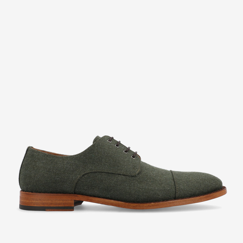 A side view of a green suede oxford shoe with brown wooden sole and black laces against a plain white background.