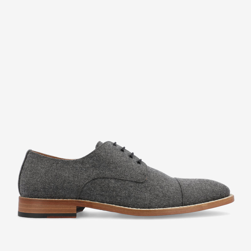 A gray, lace-up dress shoe made of felt material with a brown wooden sole and black rubber heel. The shoe features a cap toe design and minimalist stitching.