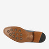 Bottom view of a leather-soled shoe with rubber traction dots, showing branding and stitching details.