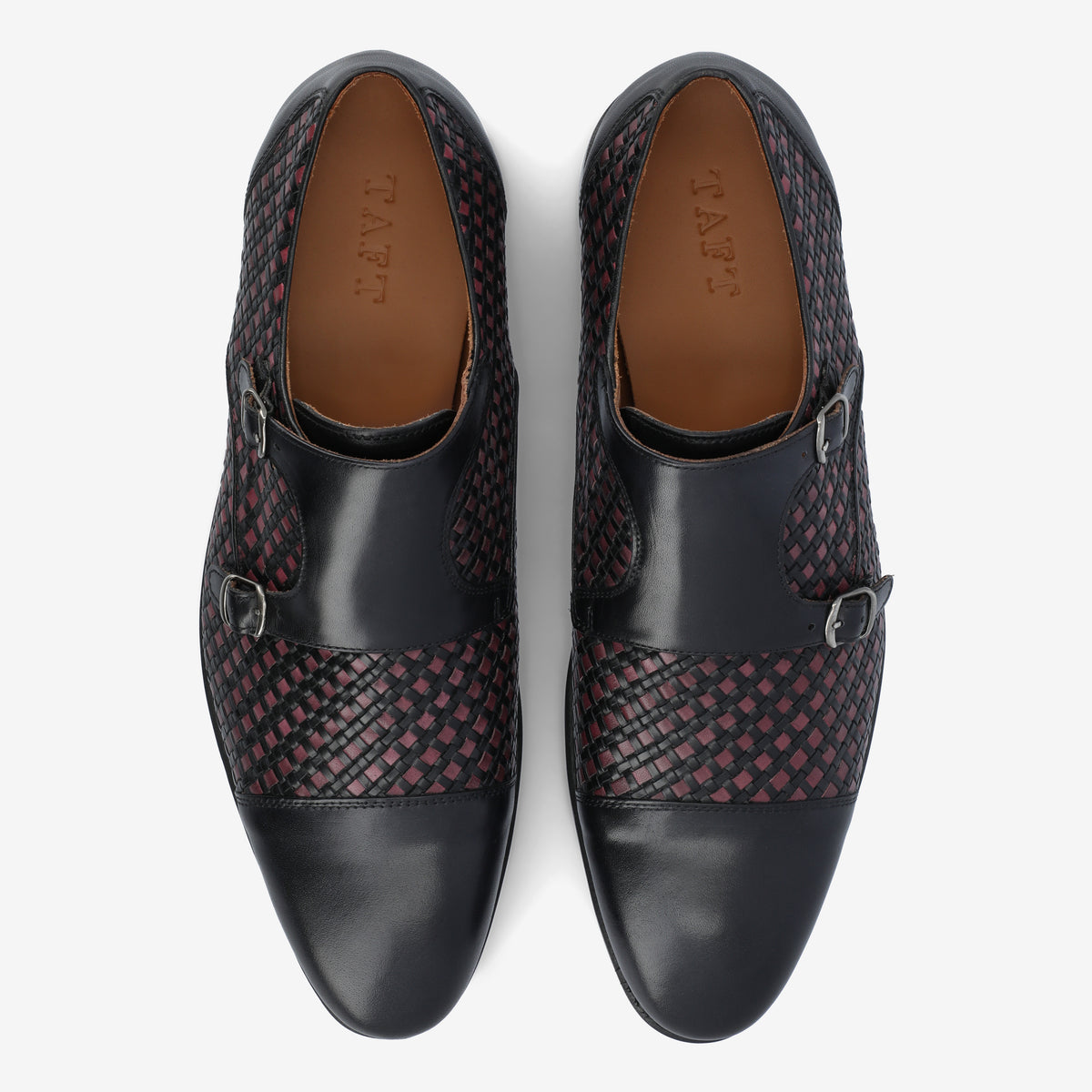 Top-down view of a pair of black dress shoes with a woven red and black pattern on the upper, two buckles on each shoe, and brown insoles.