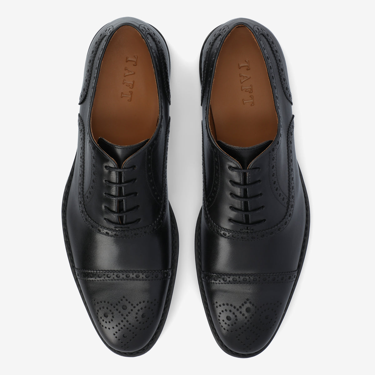 Top view of a pair of black leather dress shoes with brogue detailing and brown insoles.