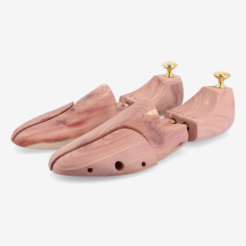 A pair of wooden shoe trees featuring a split-toe design, brass hardware, and ventilation holes, placed on a white background.