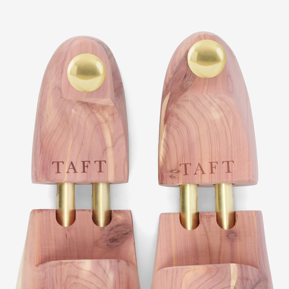 Two wooden shoe trees with brass knobs and the brand name TAFT engraved on the upper part, placed side by side on a plain white background.