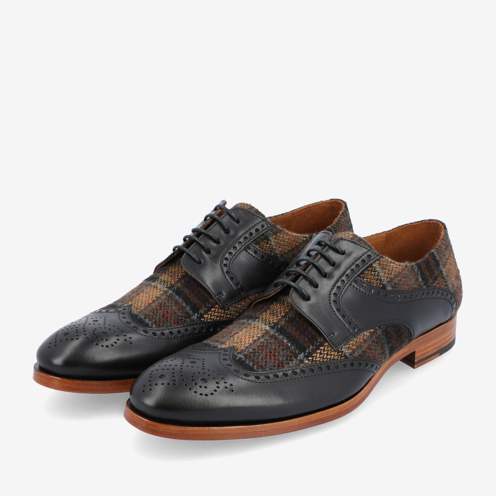 A pair of men's dress shoes with black leather accents and brown plaid fabric, featuring brogue detailing and wooden soles.