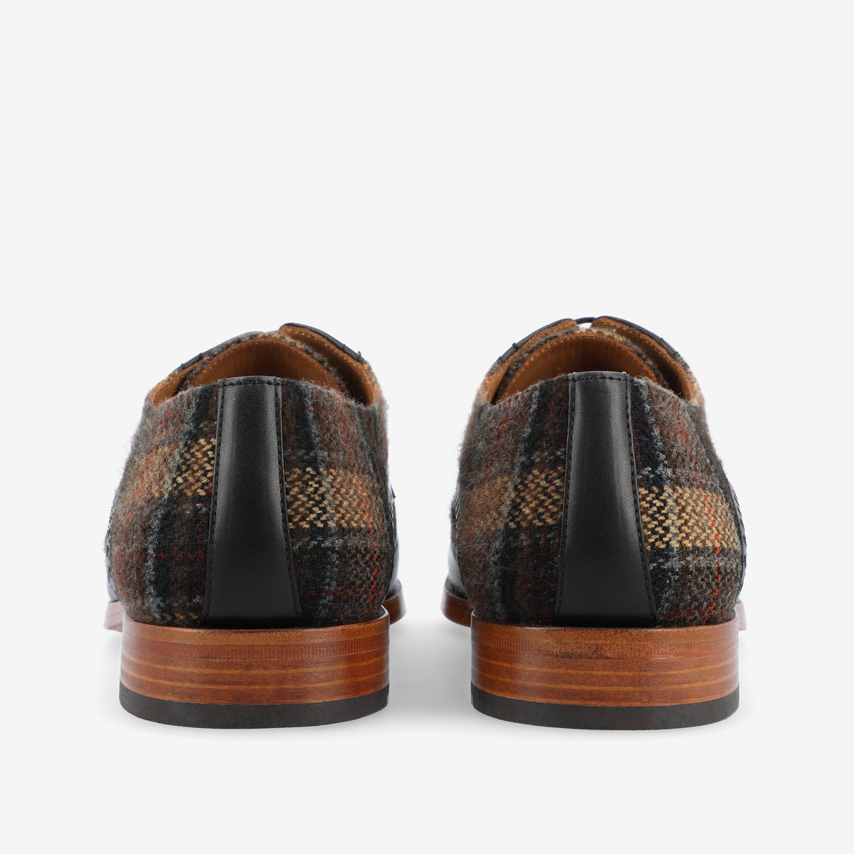 A pair of dress shoes with brown wooden soles and multicolored plaid fabric uppers viewed from the back.