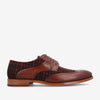 A brown and red leather and plaid brogue shoe with decorative perforations, a wooden sole, and laces, resting against a white background.